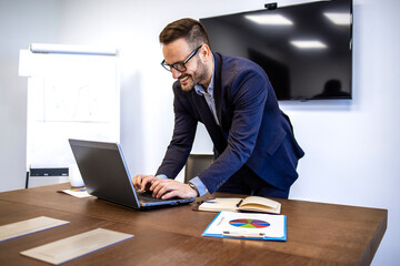 Manager in business suit typing on his laptop computer inside the company office.