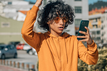 young latin hispanic man with surprised expression and mobile phone in the street