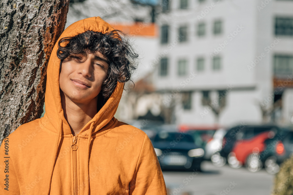 Wall mural casual teenager with sweatshirt leaning on a tree in the street