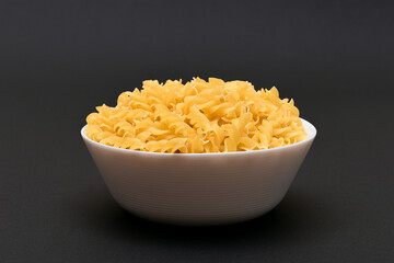 Uncooked Fusilli Pasta in White Bowl on Black Table. Raw and Dry Macaroni. Unhealthy and Fat Food. Italian Culture