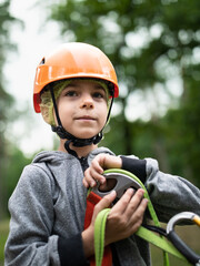 Portrait of little smiling boy in helmet and harness in sky rope park in summer
