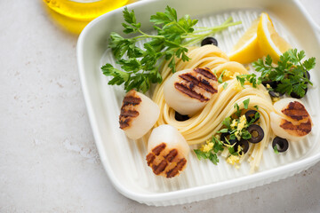 Grilled sea scallops with spaghetti, lemon zest and parsley in a beige serving pan, close-up, selective focus, horizontal shot
