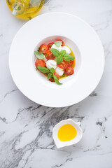 White plate with italian traditional caprese salad, vertical shot on a white marble background, view from above