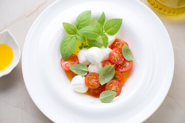 Caprese salad with mini mozzarella, cherry tomatoes, olive oil and green basil served in a white plate, middle closeup, horizontal shot