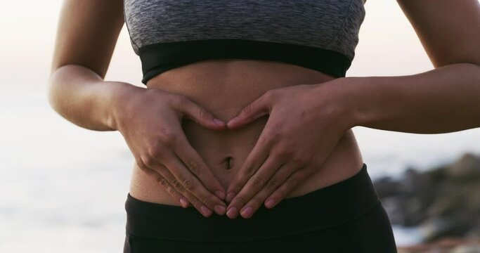 Face, stomach and woman outdoor, heart hands and diet with happiness, wellness and holistic gut. Portrait, female person and athlete with body care, beach and digestion with love symbol and abdomen