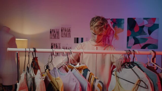 Slow motion young man in front of a hanger and trying to choose clothes in fashion design atelier