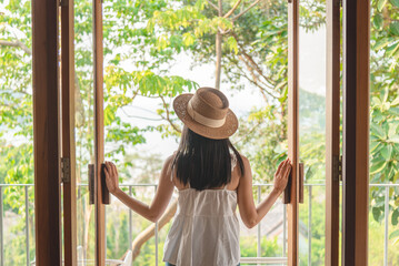 Young woman open wooden door from living room to terrace among tree and garden to relax on holiday