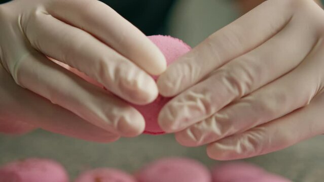 Female hands breaking almond cookies with hands breaking pink macaron cake with filling in a professional kitchen