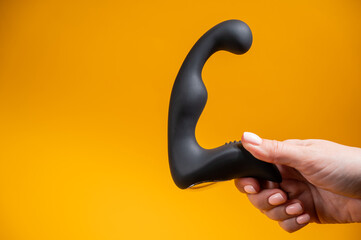 Woman holding black prostate massager on orange background. 