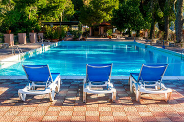 blue lounge chair in a hotel with water and swimming pool on background , vacation resort landscape of a beautiful place for holiday relax