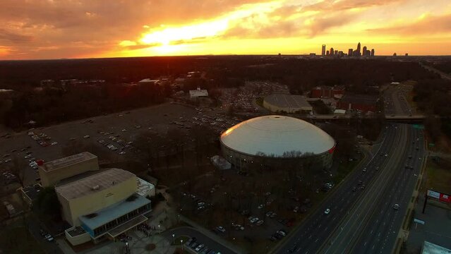 Aerial Shot Of Bojangles Coliseum By Freeway At Sunset, Drone Ascending Backward Over City Against Cloudy Orange Sky - Charlotte, North Carolina