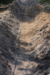long trench fire ditch made of gray brown sand outdoors in the forest