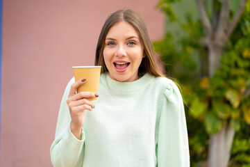 Young pretty blonde woman holding a take away coffee at outdoors with surprise and shocked facial expression