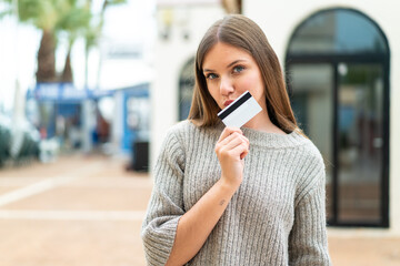 Young pretty blonde woman holding a credit card and thinking