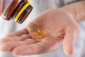 Man pouring fish oil capsules with omega 3, vitamin D in hand from medicine bottle. Nutritional supplement. Health support and treatment concept.