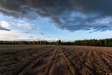Landscape with plowed agricultural field and dark clouds in the sky