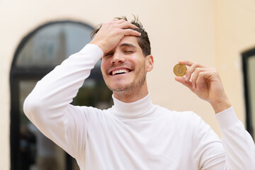 Young caucasian man holding a Bitcoin at outdoors has realized something and intending the solution