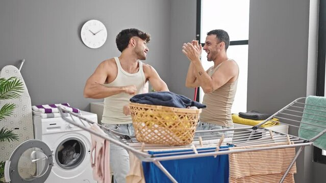 Two men couple hanging clothes on clothesline dancing at laundry room