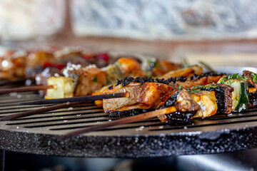 A lot of mini-kebabs of meat, fish, chicken, shrimp, vegetables on wooden skewers are fried on a small cast-iron grill