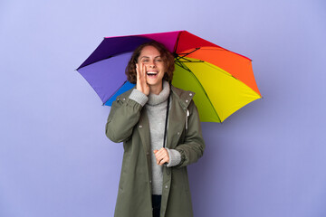 English woman holding an umbrella isolated on purple background shouting with mouth wide open