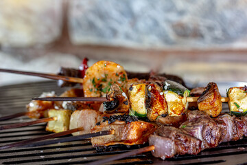 A lot of mini-kebabs of meat, fish, chicken, shrimp, vegetables on wooden skewers are fried on a small cast-iron grill