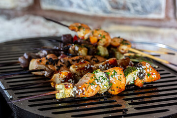A lot of mini-kebabs of meat, fish, chicken, shrimp, vegetables on wooden skewers are fried on a small cast-iron grill