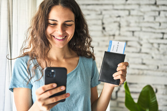 A young Caucasian woman, happily holding her phone and an airplane ticket, ready to embark on an adventure of a lifetime