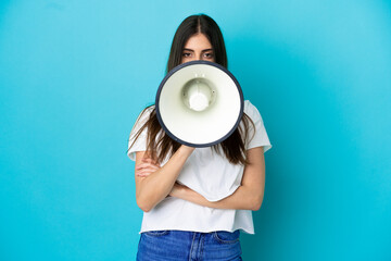 Fototapeta na wymiar Young caucasian woman isolated on blue background shouting through a megaphone to announce something