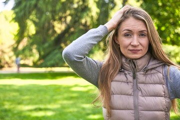 Middle-aged woman in a park on a sunny day standing with outstretched hand showing stop sign, preventing you.