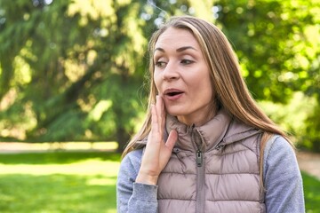 Naklejka premium Middle-aged woman in a park on a sunny day showing a copy space on a palm and holding another hand on waist.