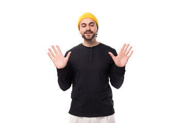 an attractive young 30-year-old guy with a beard, dressed in a black jacket and a yellow hat, shows his palms forward