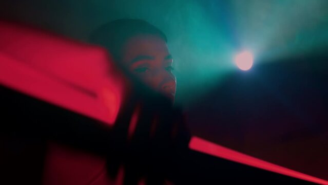 Female dancer performs modern choreography elements with red neon lightbar in arms in dark. Beautiful young woman dancing in colorful light rays in studio, moving gracefully and sensually