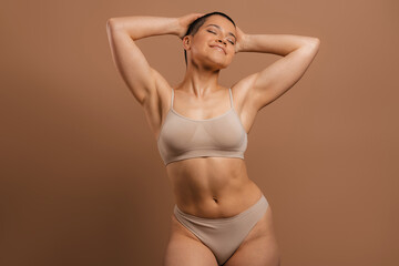 Happy young short hair woman in underwear holding hands behind head against grey background