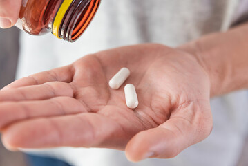 Man pouring white capsules with collagen in male hand from medicine bottle. Nutritional supplement,...