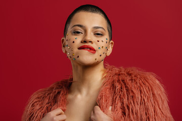 Fashionable short hair woman with shiny crystals over her face standing against red background
