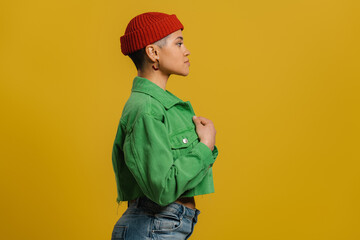Side view of fashionable young woman in hat standing against yellow background