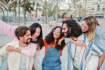 Group of young people having fun together, happy men giving their girlfriends a piggyback ride, enjoying with their best friend outside. Smiling guys carrying on shoulders their cheerful women. High