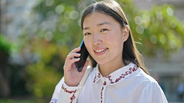 Young chinese woman talking on smartphone smiling at park