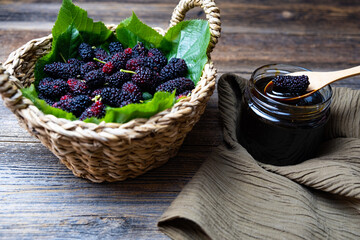 Mulberry fruit, mulberry molasses in glass bowl and fresh mulberry in basket, wooden background.