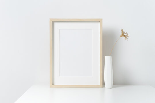 Vertical blank wooden picture frame in white interior, mockup for print, paintings or photo presentation