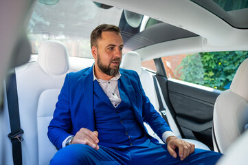 A caucasian man in a blue suit sits in the back seat of a car. Business class passenger. 