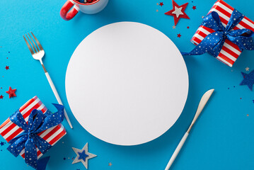 Kick off your Fourth of July party! Top-down view of festive table arrangement featuring silverware, cup, stars, confetti, gift boxes in symbolic wrapping on blue backdrop with circle for text or ads