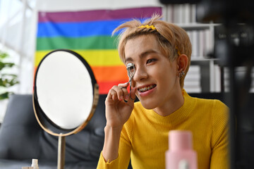 LGBT teenage boy influencer streaming online with mobile phone, Use an eyelash curler while looking at himself in the mirror.