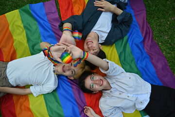 Above view with group of LGBT teenagers holding rainbow heart model while lying down on rainbow...