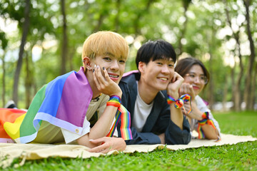 Fototapeta premium Pictured with a group of LGBT teenagers lying on the lawn, covered with rainbow flags and wearing a rainbow wristband, freedom concept, Celebration Pride month in June.
