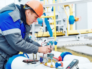 Mechanic of instrumentation and automation diagnoses sensors on the pipes of a gas distribution station with a multimeter in winter. Professional inspection and diagnostics of the working condition of