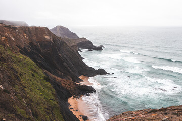 High limestone cliffs sinking into the Atlantic Ocean in the Algarve region, southwestern Portugal. Rainy weather. Wandering along the Fisherman Trail