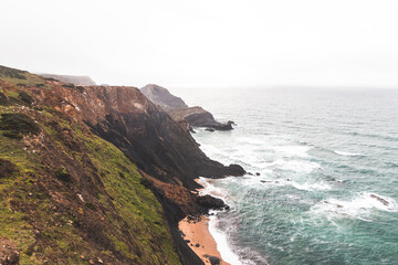 High limestone cliffs sinking into the Atlantic Ocean in the Algarve region, southwestern Portugal. Rainy weather. Wandering along the Fisherman Trail