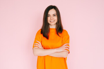 Fototapeta premium Radiant Joy: Beautiful Woman with Beaming Smile and Arms Crossed, Embracing Good Mood in Comfortable Attire - Vibrant Positivity on Pink Background.