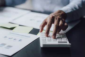 businessman or accountant hand working on calculator to calculate business data, accounting document and laptop computer at office, business concept